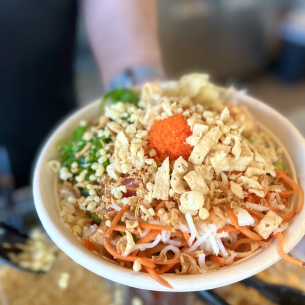 A close-up of a poke bowl with orange roe, crispy toppings, and shredded vegetables.