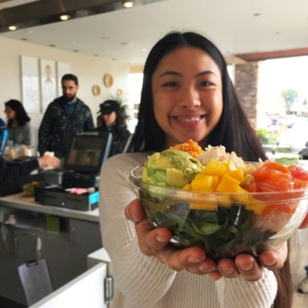 Smiling woman holding a colorful Poke Poke Fish Bar poke bowl with avocado, mango, and salmon.