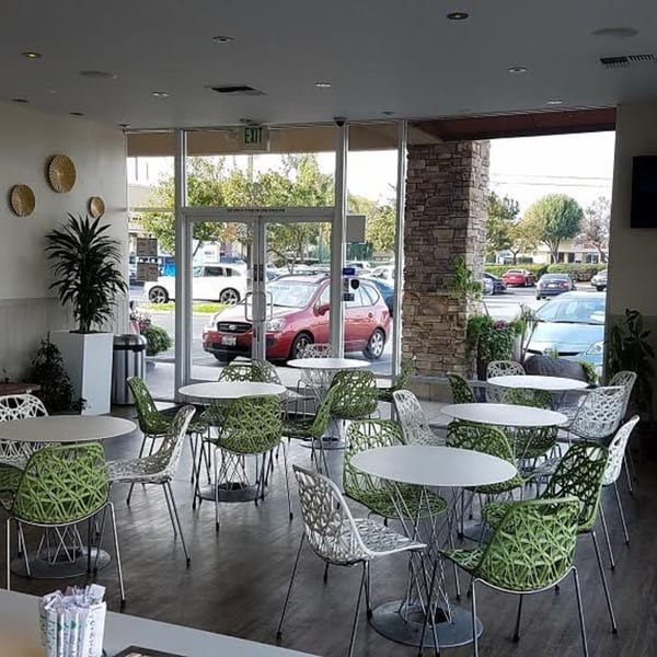 Interior of Poke Poke Fish Bar with green and white chairs, round tables, and large windows.