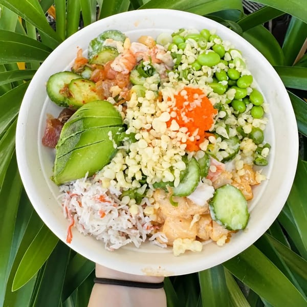 Overhead view of a colorful poke bowl with avocado, edamame, crab, and roe.
