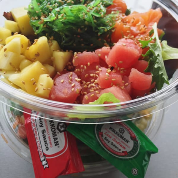 A Poke Poke Fish Bar poke bowl with tuna, salmon, pineapple, seaweed, and soy sauce packets.