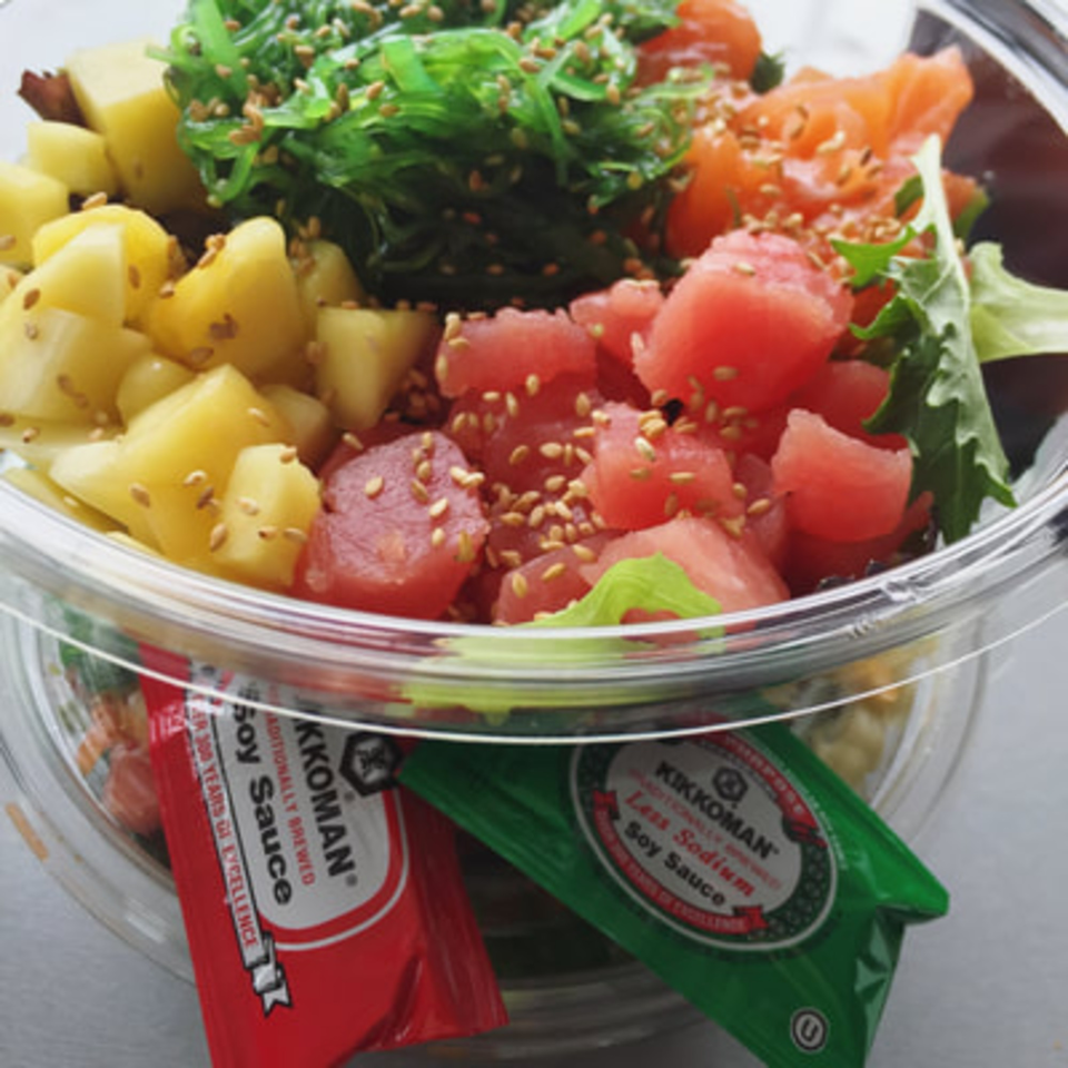 A Poke Poke Fish Bar poke bowl with tuna, salmon, pineapple, seaweed, and soy sauce packets.