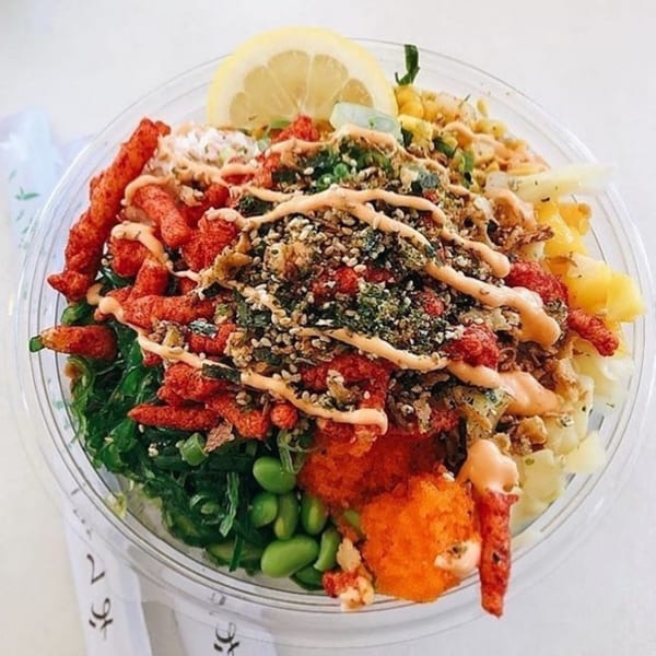 A colorful poke bowl with Hot Cheetos, seaweed, edamame, fish roe, and a lemon slice.