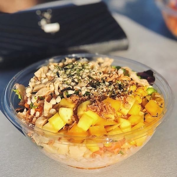 A vibrant Poke Poke Fish Bar poke bowl with mango, rice, and various toppings in a clear container.