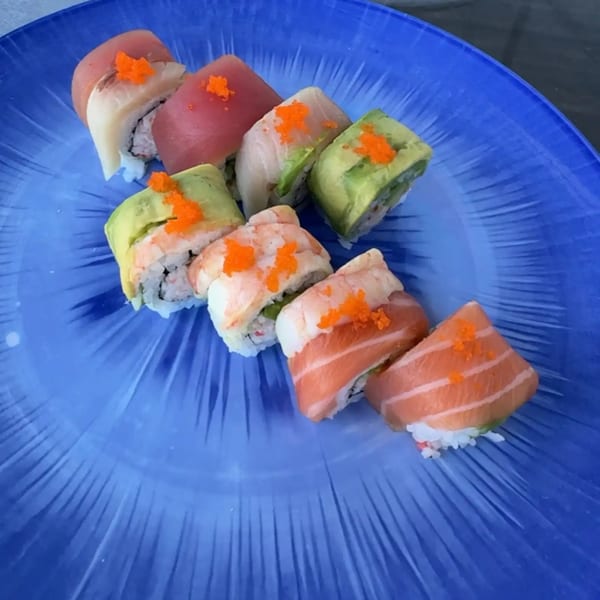 Assorted sushi rolls with tuna, salmon, shrimp, and avocado, topped with orange roe on a blue plate.