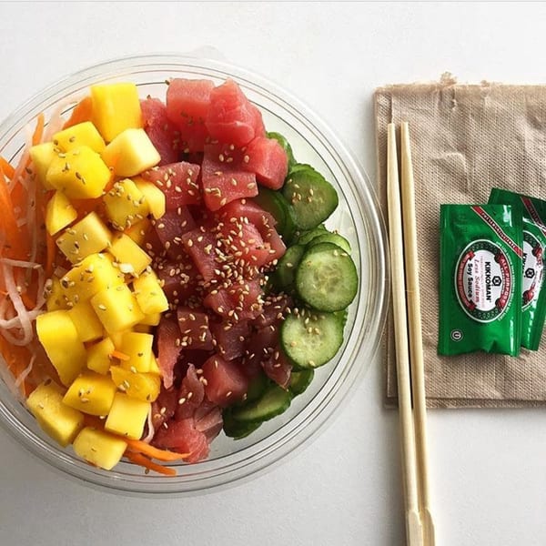 Poke bowl with tuna, mango, cucumber, and carrots, with chopsticks and soy sauce packets.
