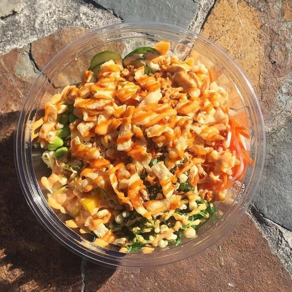 Poke bowl with crispy toppings and orange sauce, on a stone surface.