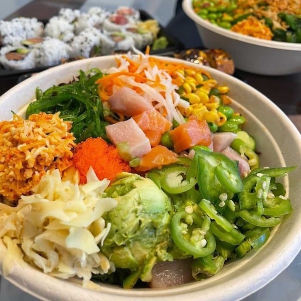 Close-up of a colorful Poke Poke Fish Bar poke bowl with various toppings and sushi in the background.