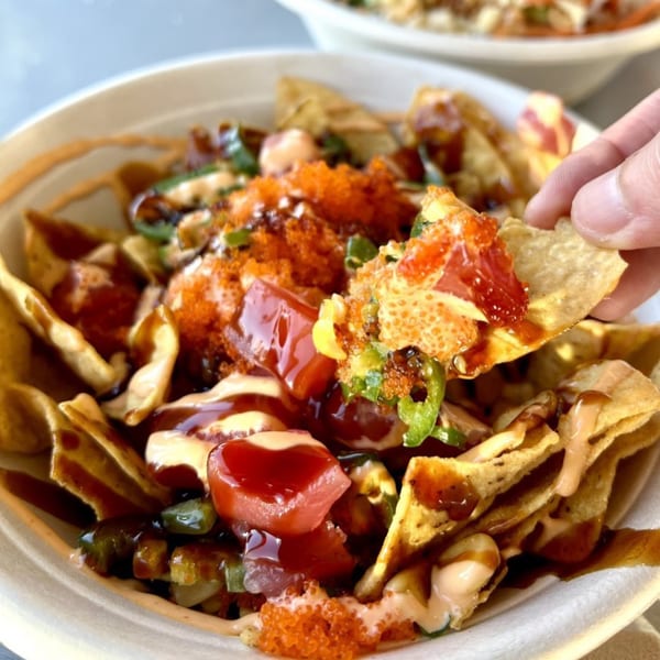 A hand picks up a chip from a bowl of Poke Poke Fish Bar nachos with tuna and roe.