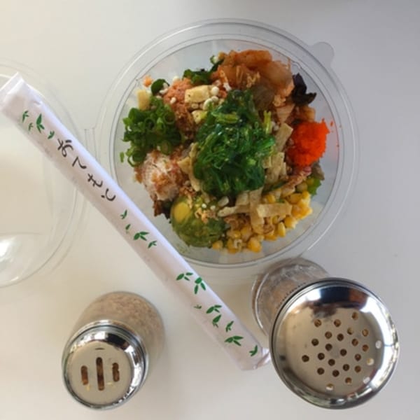 Overhead view of a colorful poke bowl with chopsticks, salt, and pepper shakers.