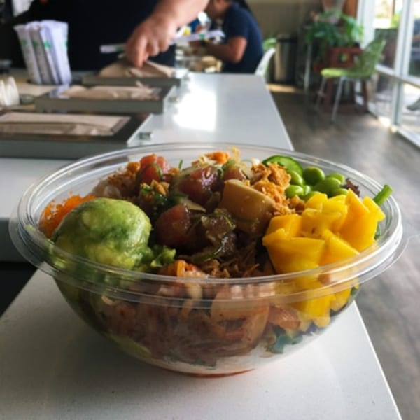 A colorful poke bowl with mango, avocado, edamame, and various fish on a white counter.