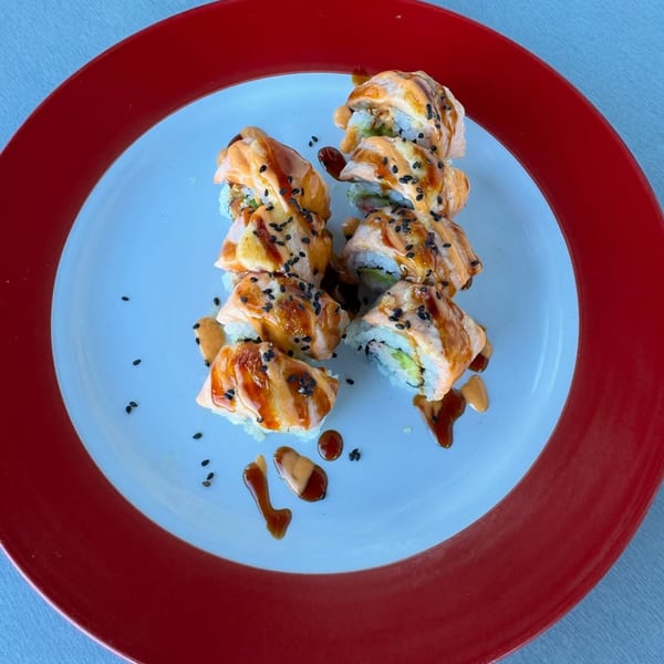 Two rows of Poke Poke Fish Bar sushi rolls with sauce and sesame seeds on a red and white plate.